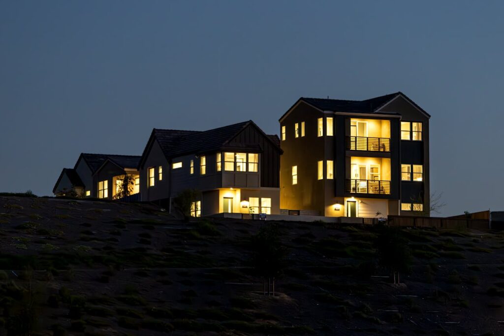 Brightly lit modern house on a hill at dusk, showcasing urban residential architecture.